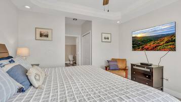 A bedroom with a bed, a television, a ceiling fan, and a door leading to a bathroom.