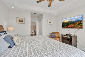 A bedroom with a bed, a television, a ceiling fan, and a door leading to a bathroom. - Mountain Views + Walk to Overlook Barn, Slopes, Fred's & White Wolf! (Banner Elk)