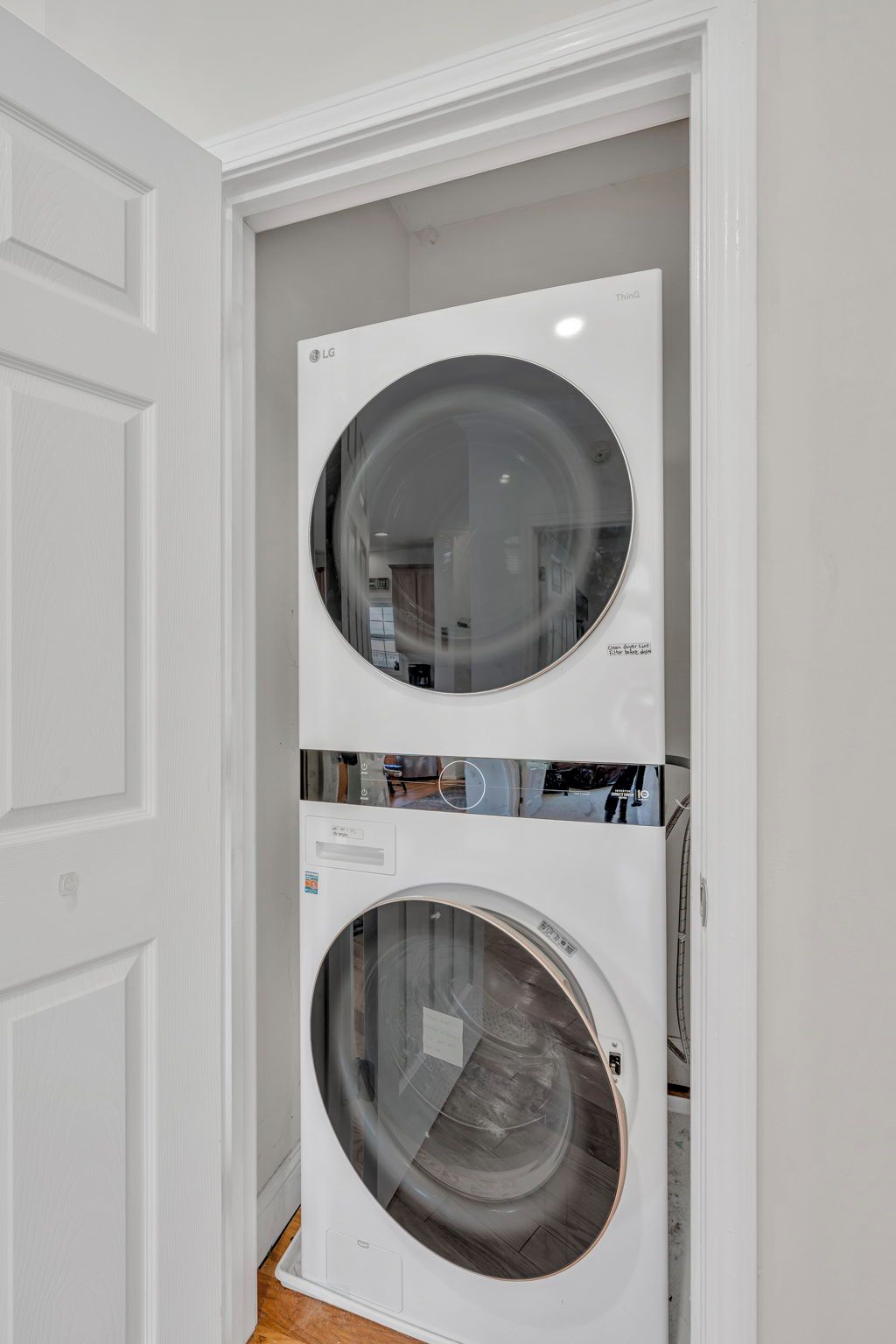 A wall-mounted washer and dryer unit with a reflective circular door, installed in a white-walled room with a wooden floor.