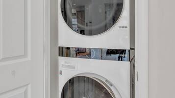 A wall-mounted washer and dryer unit with a reflective circular door, installed in a white-walled room with a wooden floor.