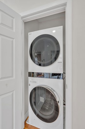 A wall-mounted washer and dryer unit with a reflective circular door, installed in a white-walled room with a wooden floor. - Mountain Views + Walk to Overlook Barn, Slopes, Fred's & White Wolf! (Banner Elk)
