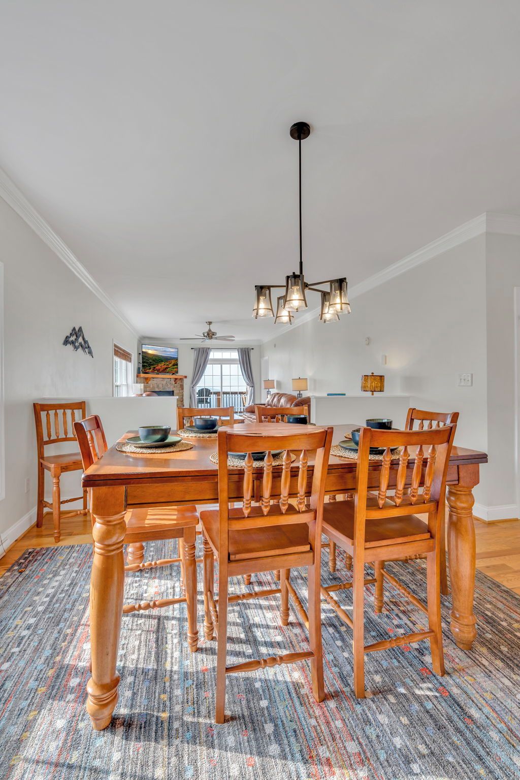A dining area with a wooden table and chairs, a patterned rug, and a modern chandelier.