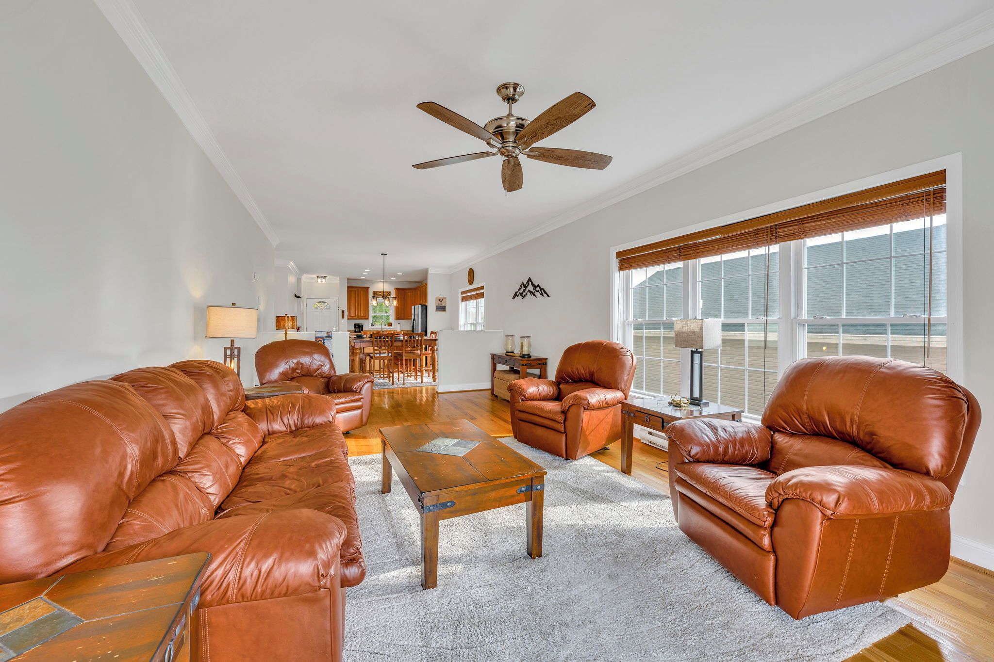 A spacious living room with leather sofas, a coffee table, and a ceiling fan.