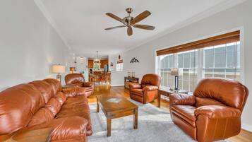 A spacious living room with leather sofas, a coffee table, and a ceiling fan.