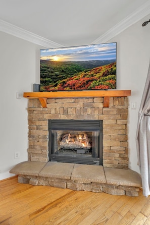 A fireplace with a stone surround, a flat-screen TV mounted above it, and a wooden shelf.