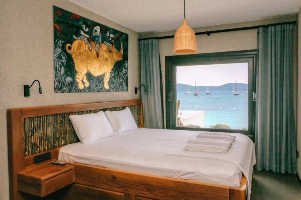 A hotel room with a large bed, a painting of a bull, a view of the sea, and a wooden headboard.