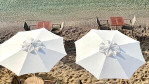 Ein Strand mit klarem Wasser, zwei weißen Sonnenschirmen und Holzstühlen.