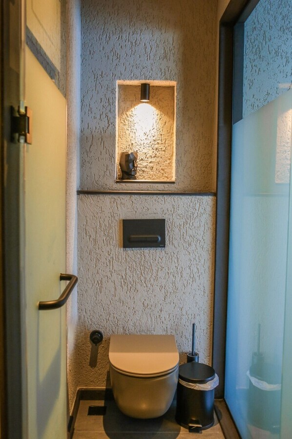 Un bagno compatto con toilette, bidet e un piccolo ripiano con un punto luce.