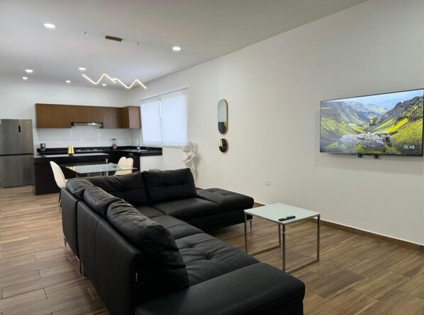 Relax in this stylish living space with a black leather sofa, flat-screen TV, and dining area.
