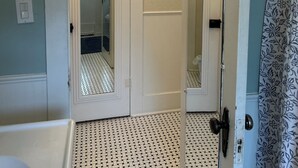 Un baño con puerta blanca, espejo, candelabro y piso estampado.