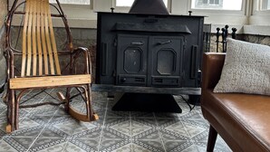 Una habitación con un gran horno de leña, un sillón mecedor de madera, un sofá con un cojín y baldosas de suelo con diseño.