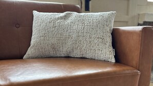 Un sofá de cuero marrón con un cojín blanco con textura.