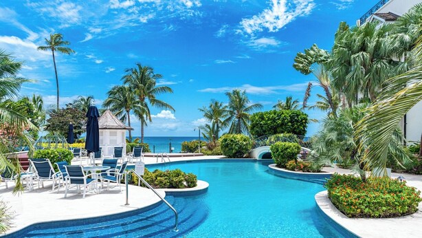 A pool area with lounge chairs, palm trees, and a view of the ocean. - Exclusive one bedroom apartment, a few steps from the Caribbean Sea (Speightstown)