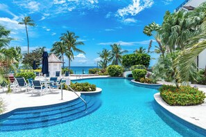 Un área de piscina con sillones de descanso, palmeras y vista al océano.