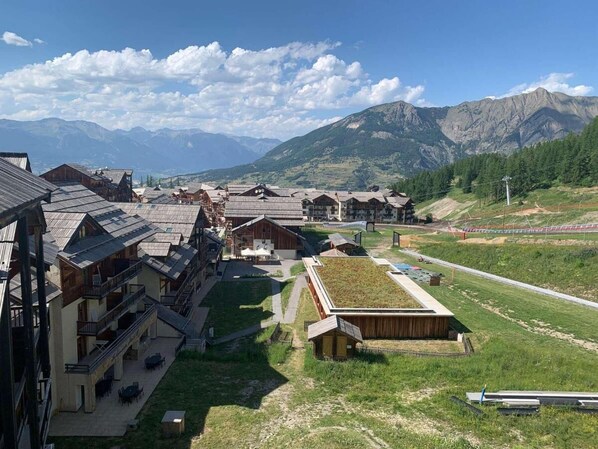 A mountain resort with chalet-style buildings, a green-roofed structure, and a view of distant mountains. - 200m from resort center, 3rd floor, swimming pool, balcony, tv, ski locker, 24m², Les Orres (Les Orres)