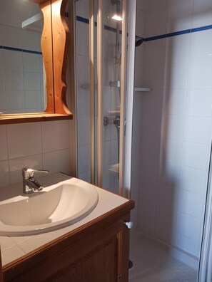 A bathroom with a wooden vanity, a white sink, a glass shower enclosure, and a mirror.