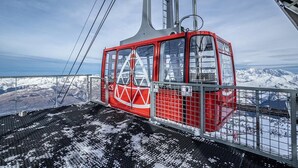 Un teleférico rojo con estructura metálica, suspendido por cables, con vistas a un paisaje montañoso nevado.