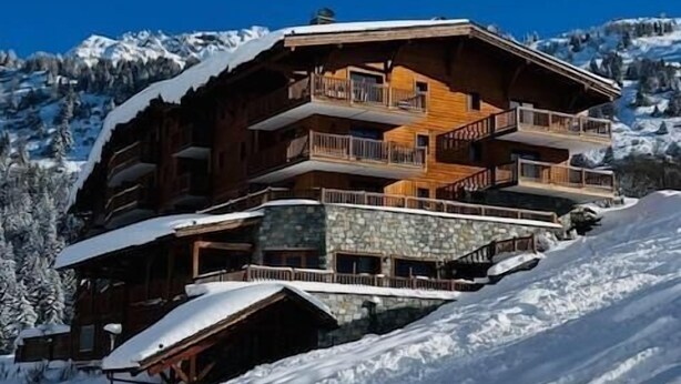 Una cabaña de madera de varios pisos con balcones, con el paisaje nevado de una montaña al fondo.