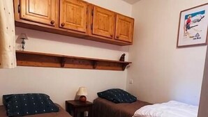 Una habitación con dos camas, armarios de madera arriba y un cuadro en la pared.