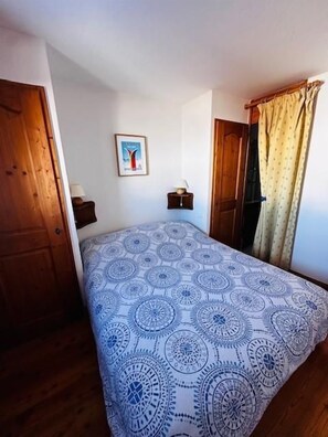 A bedroom with a patterned bedspread, a framed picture on the wall, and wooden doors.