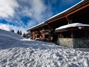 Eine Holzhütte mit steinernen Fundamenten, umgeben von verschneitem Gelände und Bäumen.