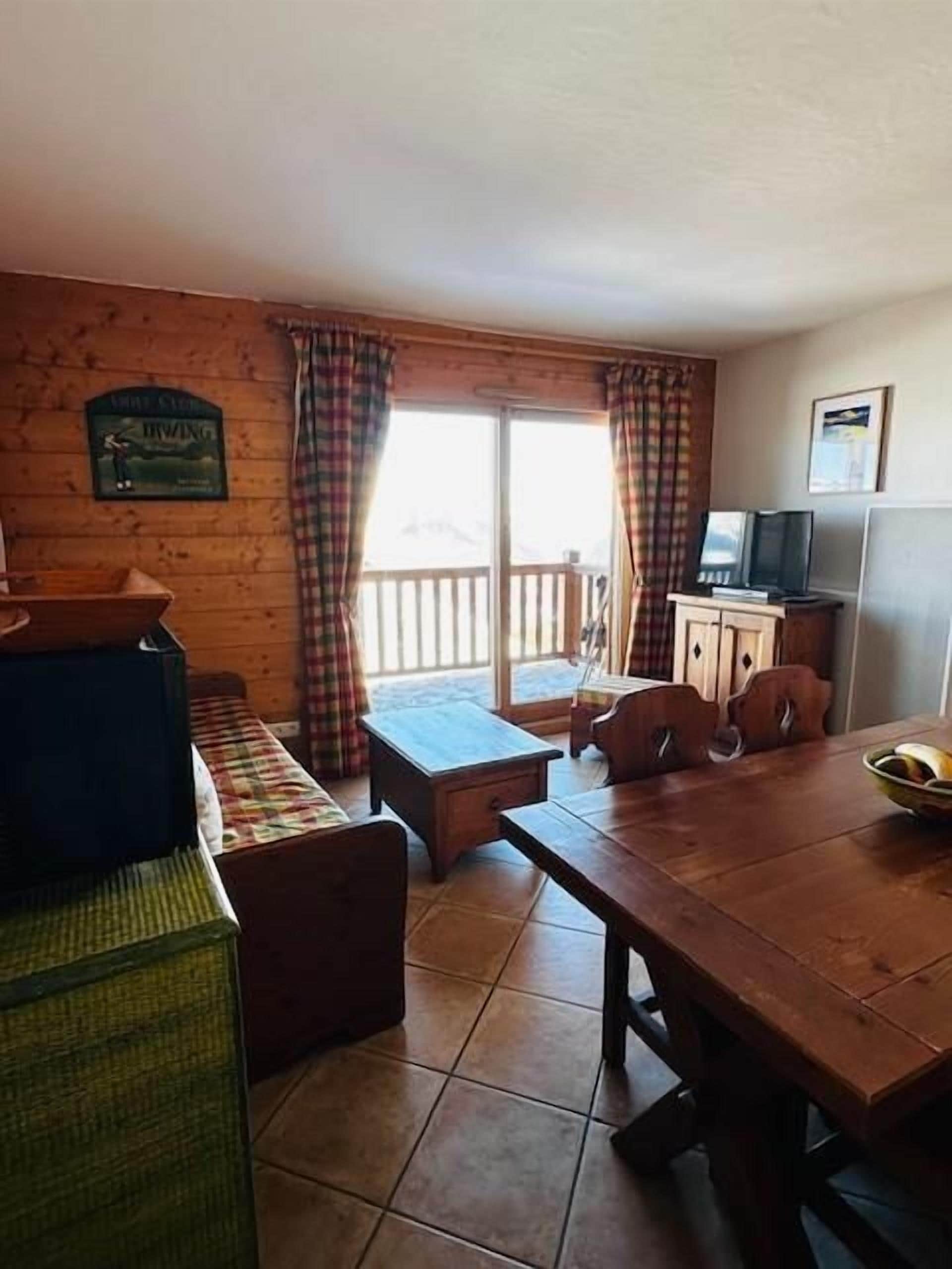 Una habitación acogedora con una mesa de madera, una banca y un televisor sobre un mueble.