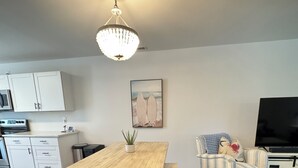 A modern living room with a wooden dining table, a striped armchair, a TV, and a kitchen area with white cabinets.
