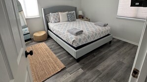 A bedroom with a bed, bedside tables, a wall-mounted TV, and a window.
