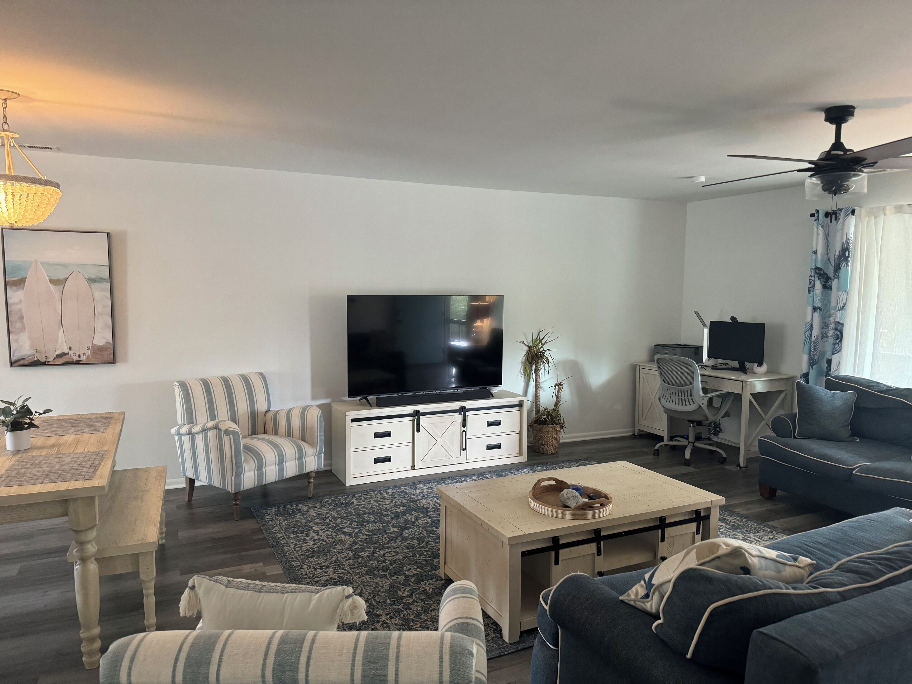 Una sala moderna con una televisión de pantalla plana, sillones a rayas, un sofá, una mesa de centro y un escritorio con una computadora.