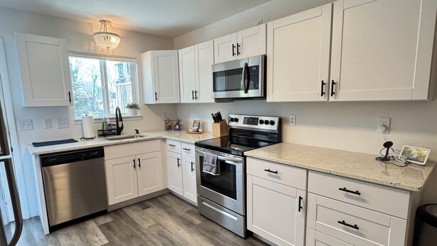 A modern kitchen with white cabinets, stainless steel appliances, and a wooden floor.