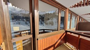 Een balkon met houten leuningen en grote ramen met uitzicht op een besneeerd landschap.