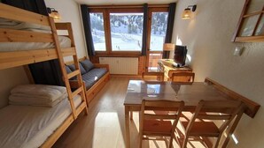 Een gezellige kamer met een stapelbed, een houten tafel met stoelen, een bank en een televisie.