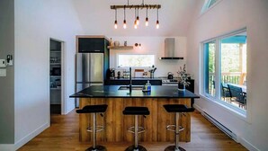 A modern kitchen with a central island, bar stools, and a hanging light fixture. - Hôtel à la maison - La Villa Foresta (Coaticook)