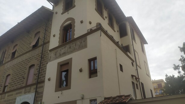 Ein mehrstöckiges Gebäude mit einer Kombination aus Ziegel- und Putzfassaden, mit Rundbogenfenstern und einem Balkon.
