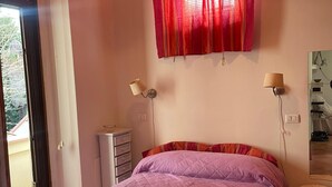 Ein Schlafzimmer mit einem Bett, einem Fenster mit roten Vorhängen, einem Schminktisch und zwei Wandlampen.