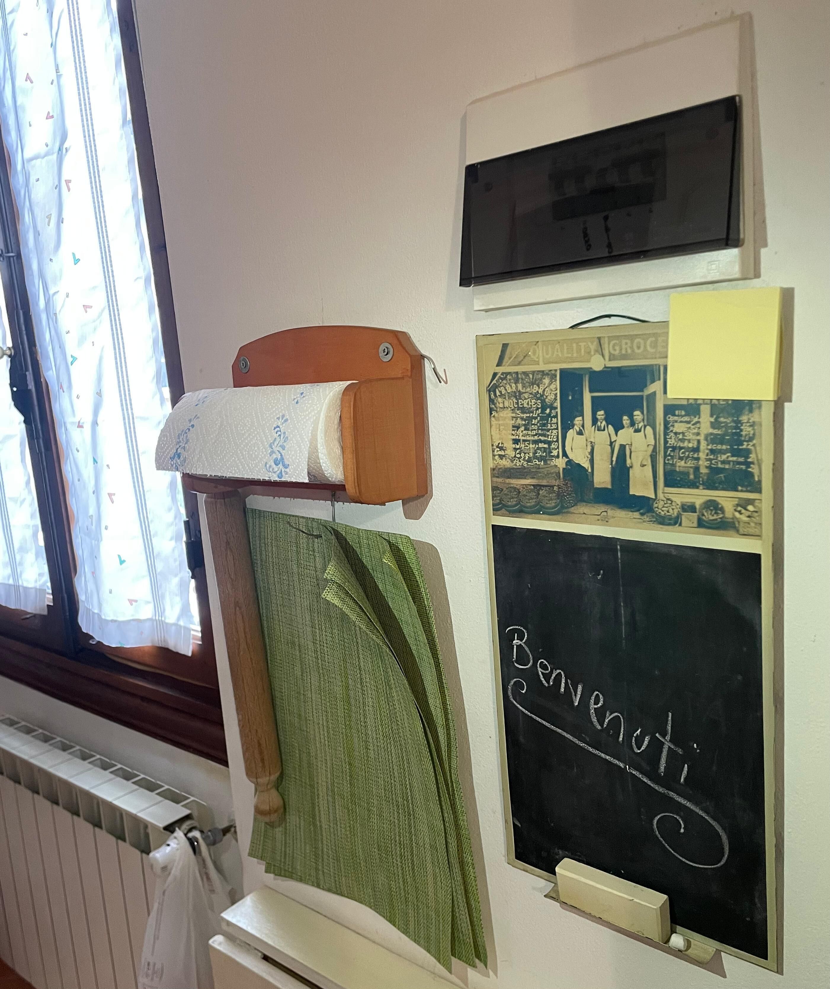 Une pièce avec un radiateur, un tableau noir couvert d’écritures manuscrites, une enseigne ancienne et une fenêtre avec des rideaux.