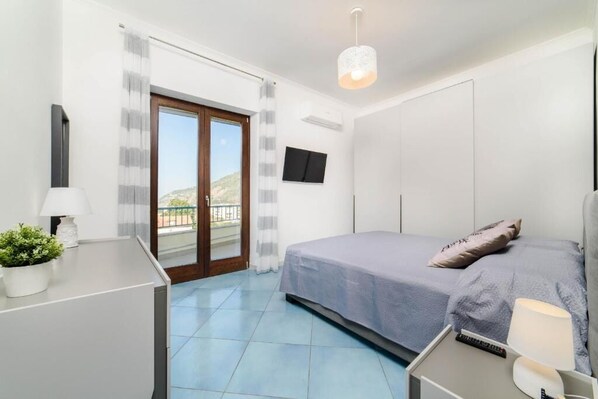A bedroom with a bed, a desk, a TV, and a balcony.