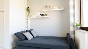 A modern living room with a grey sofa, a small side table, and a wall-mounted shelf with decorative items and a sign that says "ENJOY".
