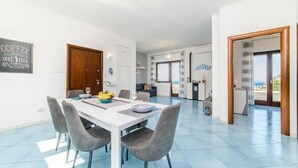 A spacious living area with a dining table, grey upholstered chairs, and a kitchen in the background.