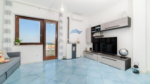 A spacious living room with a large TV, a grey sofa, and a dining area with a modern kitchen unit.