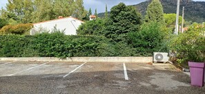A parking area with a white building and dense greenery in the background. - Apartment T2 duplex le Cocon de Saint Clair with beautiful sea view (Le Lavandou)