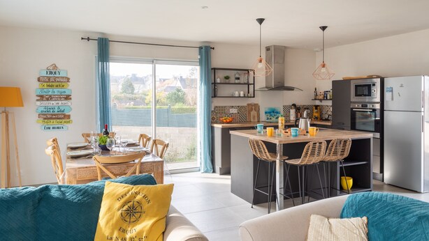 A modern kitchen with a central island, bar stools, and a dining area with a table and chairs. - Côte et mer - Proche plage, parking privé (Erquy)