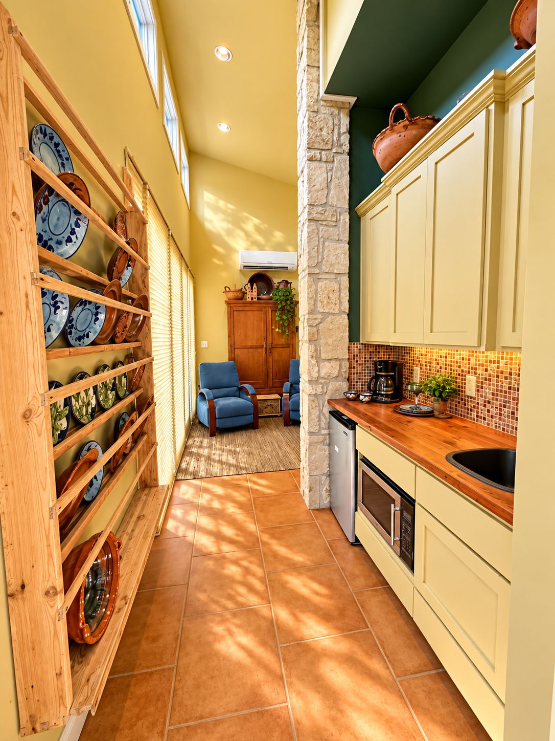 A kitchen with a stone accent wall, wooden shelving with dishes, and a tiled floor.