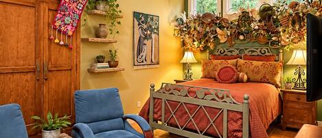 Une chambre à coucher avec un lit, deux fauteuils bleus, une armoire en bois, un ventilateur de plafond et une fenêtre donnant sur un paysage verdoyant.