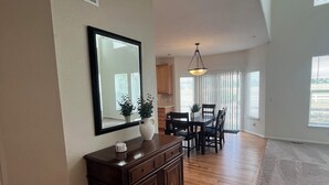 A spacious living room with hardwood flooring, a dark wooden cabinet, a large mirror, and a dining area with chairs and a table. - Spacious 5BR Retreat by Trails Pet-Friendly (Parker)