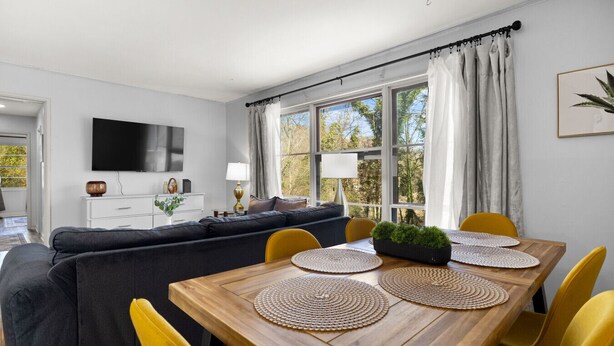 A modern living room with a sofa, a dining table with yellow chairs, and a TV mounted on the wall. - Cozy Home in Oak Ridge w/ 3BR (Oak Ridge)