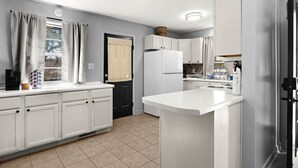 A modern kitchen with white cabinetry, a built-in island, a black refrigerator, and a window with curtains. - Cozy Home in Oak Ridge w/ 3BR (Oak Ridge)