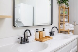A bathroom with two sinks, a mirror, and a wooden shelf with towels.