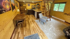 Interior acogedor de una cabaña con comedor, cocina y habitación doble en altillo con escalera de madera.