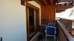 A balcony with wooden railings, a sliding glass door, and two blue chairs.